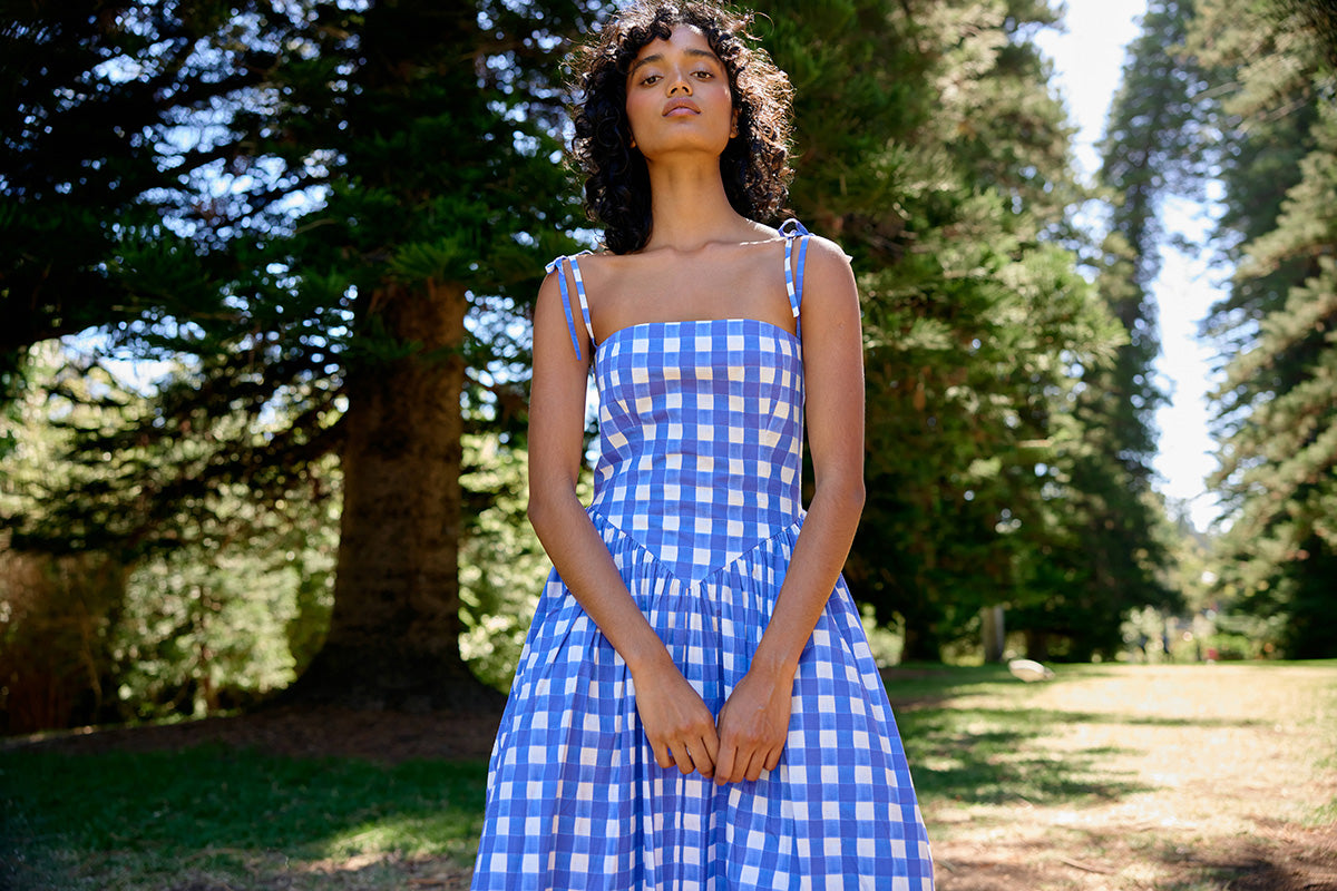 Woman wearing a blue checkered dress standing in a park with trees in the background