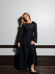 Model wearing the Odile Gown in Noir, a black silk-cotton maxi dress with a rosette at the shoulder