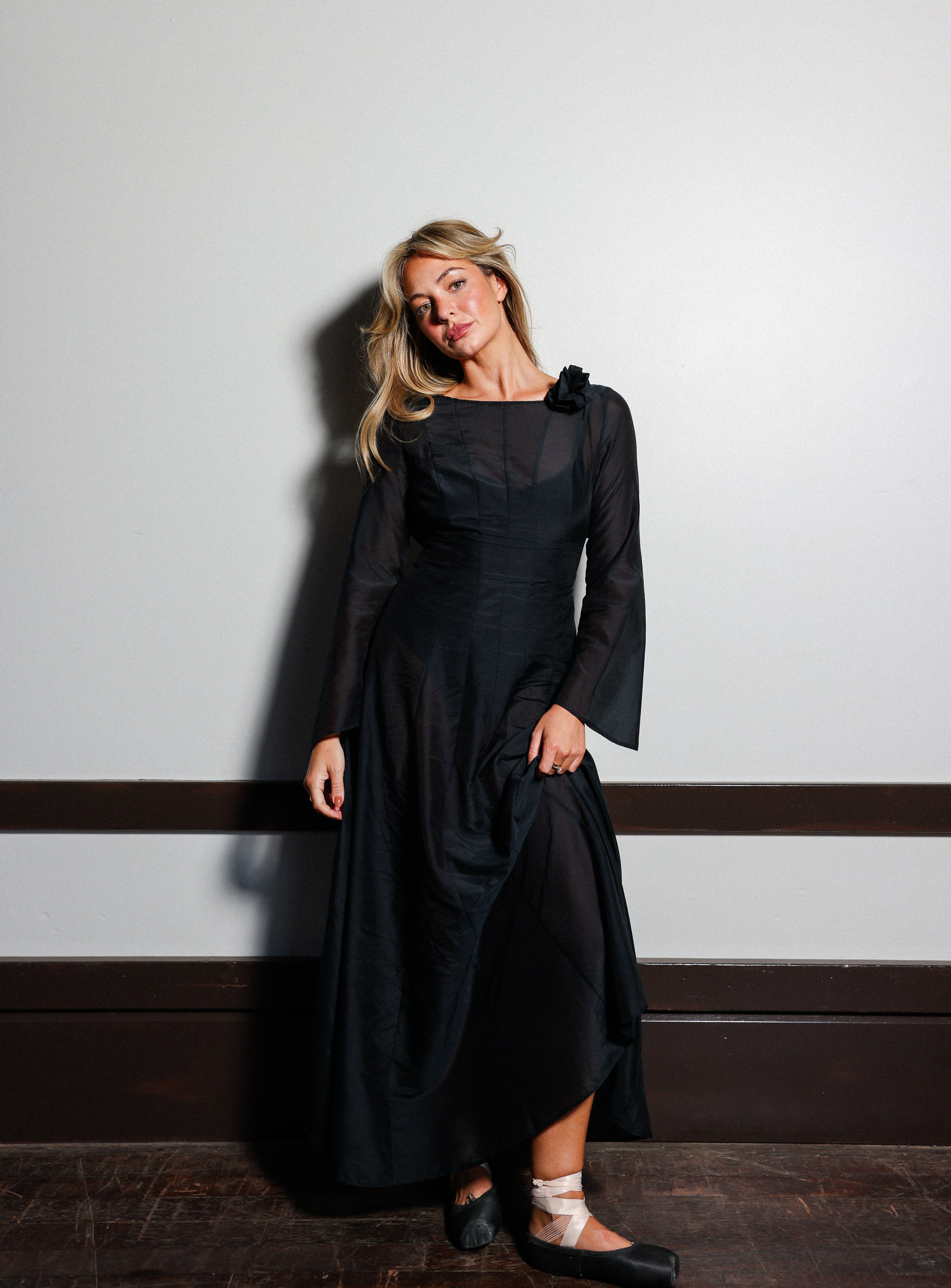 Model wearing the Odile Gown in Noir, a black silk-cotton maxi dress with a rosette at the shoulder