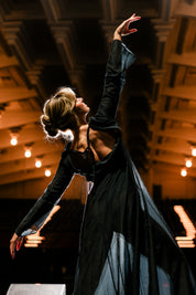 Dancer in the Odile Gown, a sheer black long sleeve evening gown, arms raised on stage